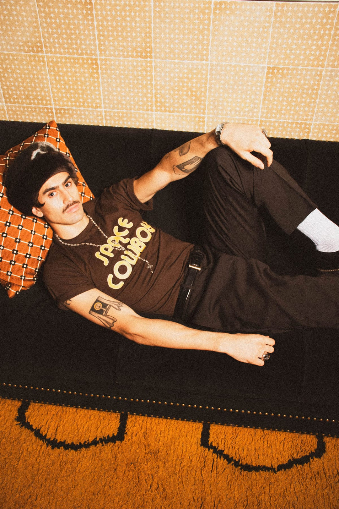 Model in vintage Space Cowboy graphic tee lounging on retro orange couch with 70s interior styling