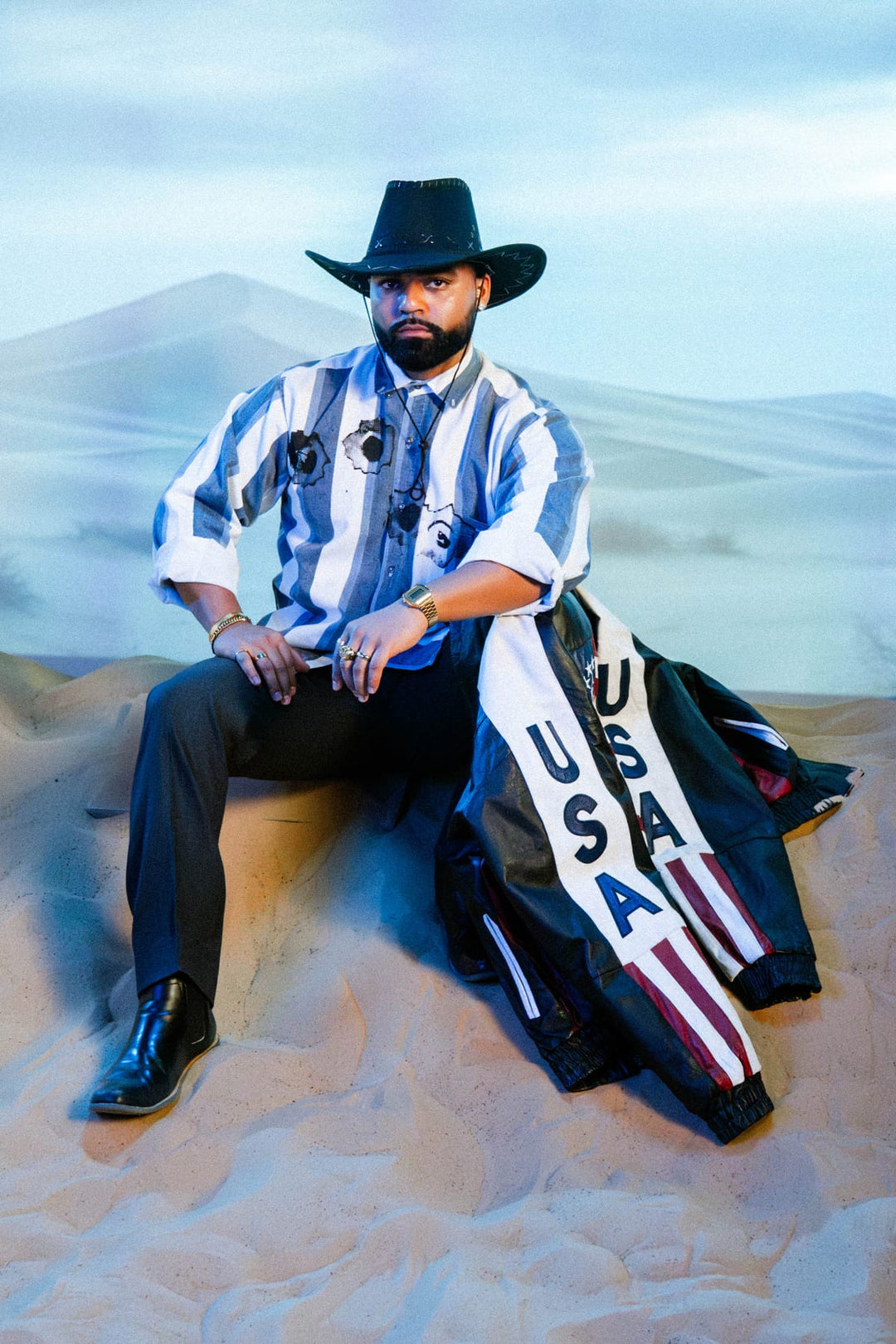 Styled model in vintage striped shirt and cowboy hat with USA leather jacket on desert set in Miami studio