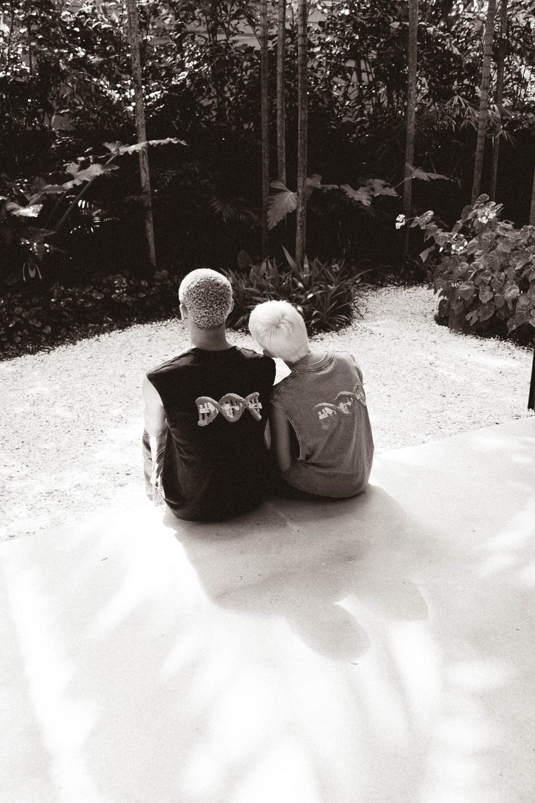 Two people wearing DNA Originals merch sitting together in a lush Miami garden setting