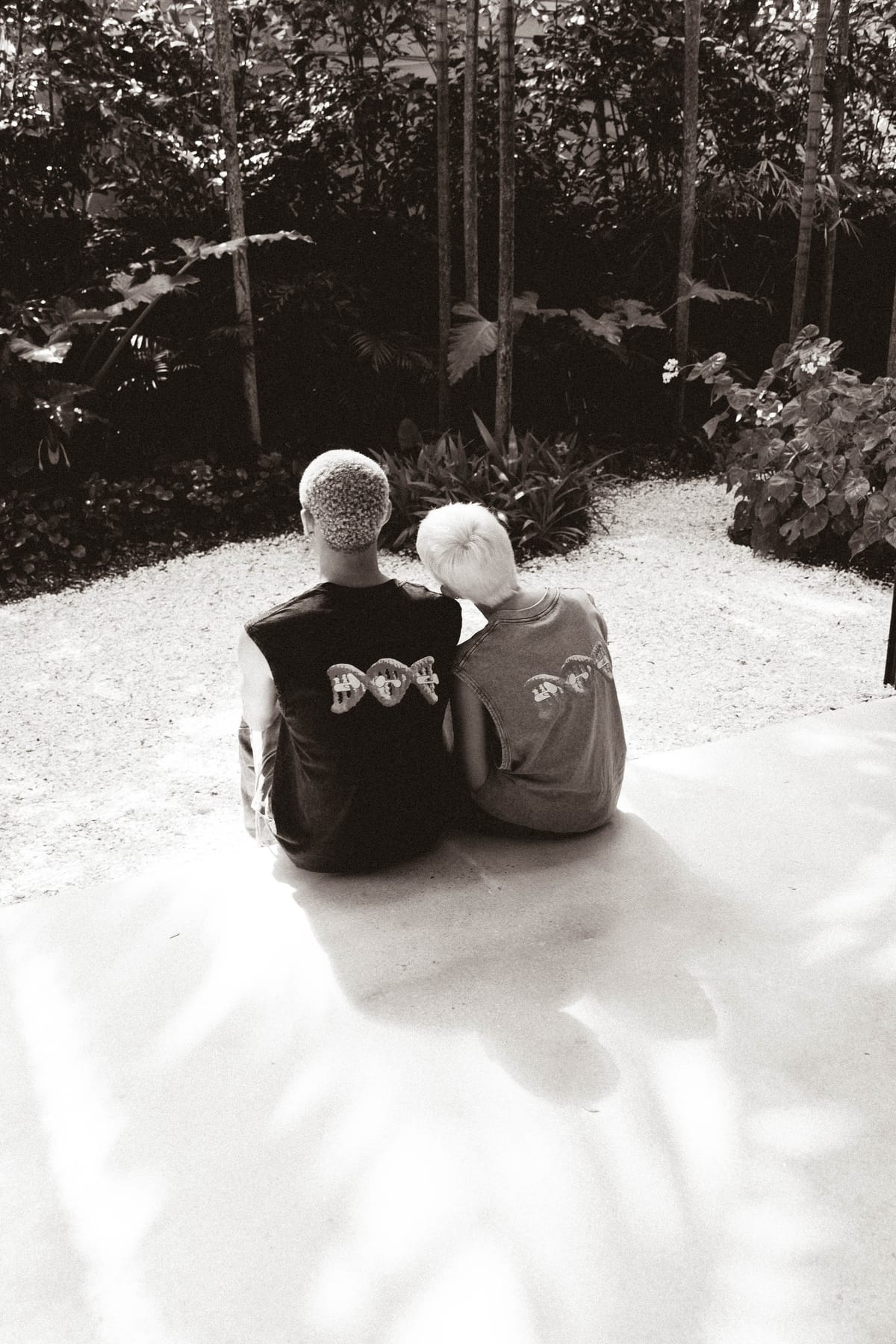 Two people wearing DNA Originals merch sitting together in a lush Miami garden setting