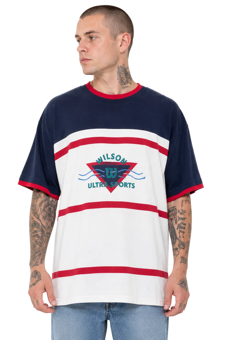 A man wearing a Wilson Ultra Sports short-sleeve t-shirt with navy blue, white, and red horizontal stripes, featuring a red and blue geometric logo on the chest.