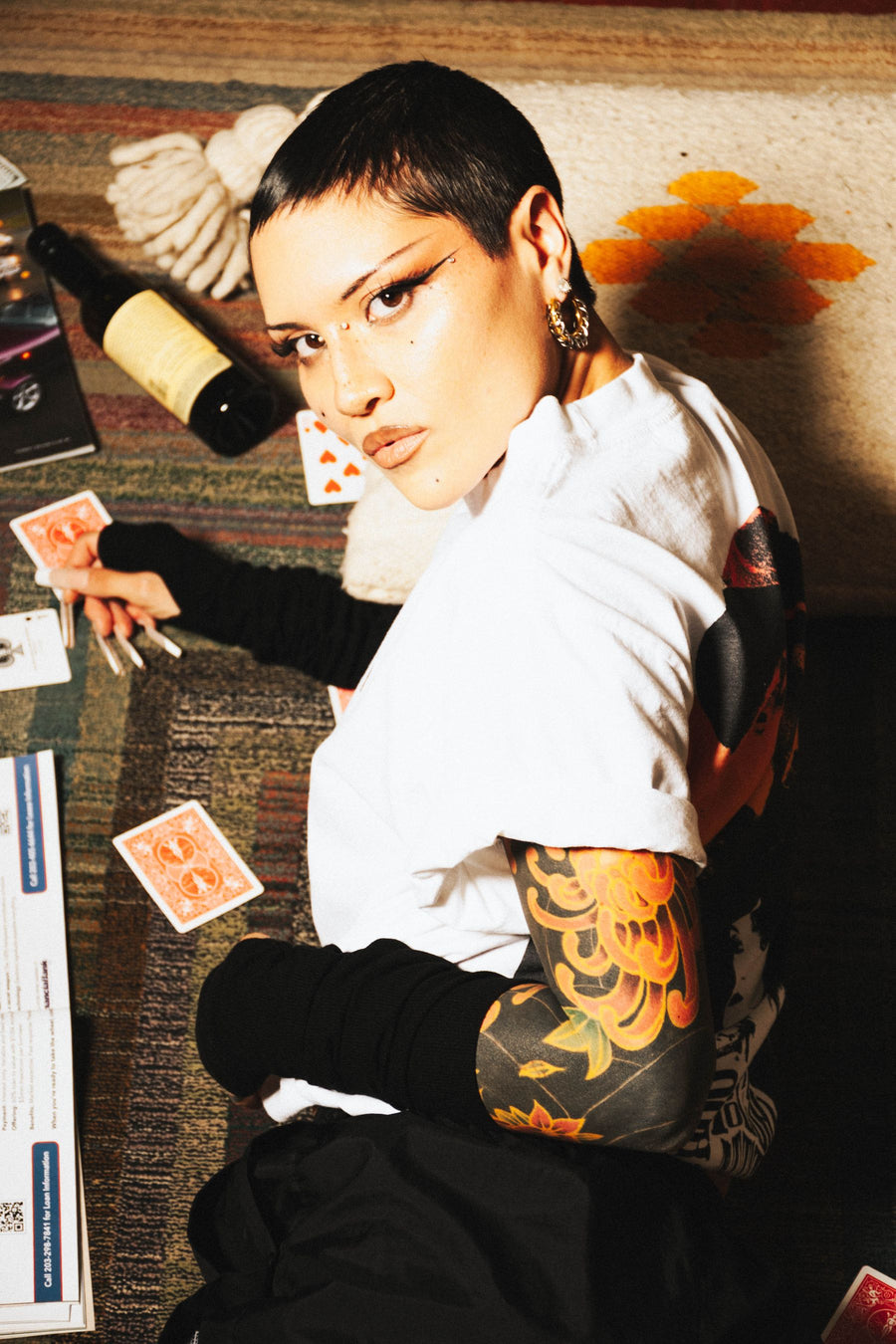 Short hair, tattoo sleeve and a white tee among playing cards