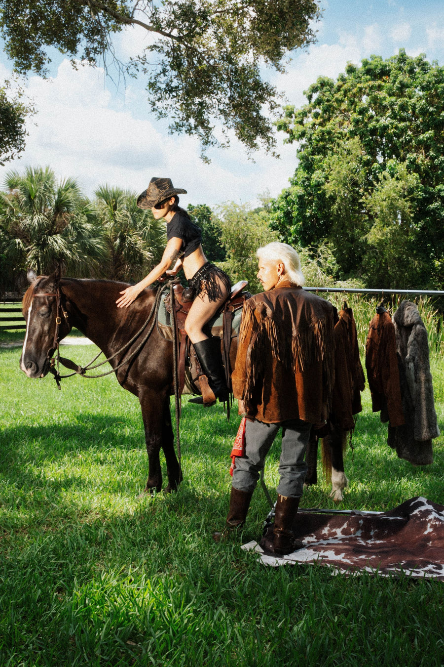 On horseback in a cowboy hat, beside a rack of suede jackets