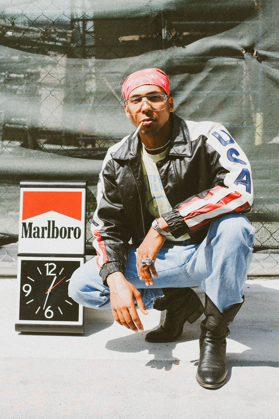 Crouched by a vintage Marlboro clock in a leather USA jacket and red bandana