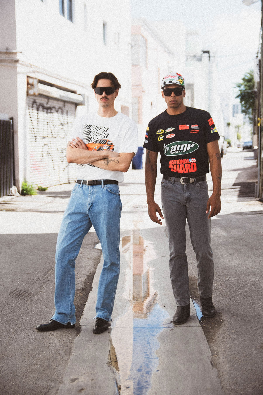 Two friends in an alley in vintage NASCAR tees and straight-leg jeans